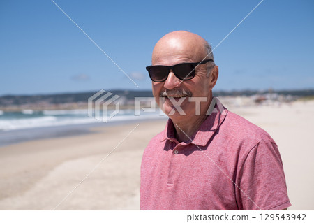 An elderly man with a mustache walking on the beach, enjoying his vacation. 129543942