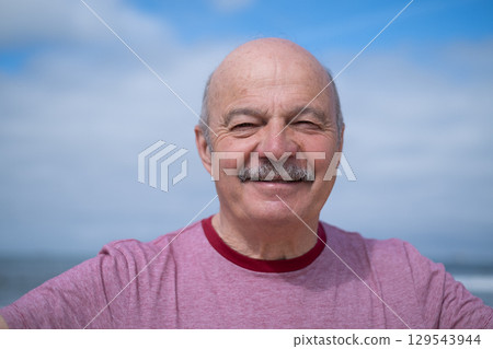 An elderly man with a mustache walking on the beach, enjoying his vacation. 129543944