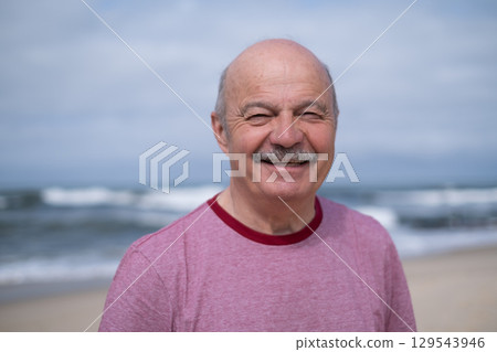 An elderly man with a mustache walking on the beach, enjoying his vacation. 129543946