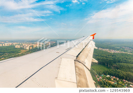 View of airplane wing, blue skies and green land during landing. Airplane window view. View of airplane wing, blue skies and green land during landing. Airplane window view. 129543969