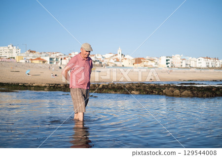 An elderly man with a mustache walking on the beach, enjoying his vacation. 129544008