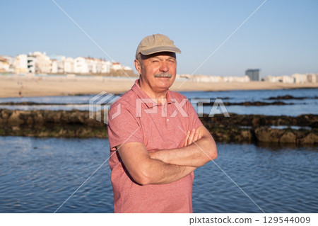 An elderly man with a mustache walking on the beach, enjoying his vacation. 129544009
