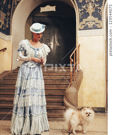Elegant woman standing with fluffy Pomeranian dog near arched doorway Elegant woman standing with fluffy Pomeranian dog near arched doorway 129544073