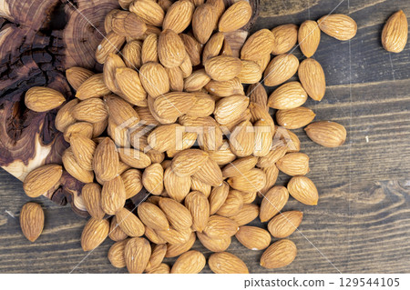 dried almonds scattered on a wooden table, edible delicious and crunchy brown almonds, closeup dried almonds scattered on a wooden table, edible delicious and crunchy brown almonds, closeup 129544105