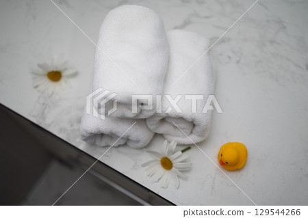 Soft Rolled Towels and a Rubber Duck With Daisies Arranged on a Marble Surface 129544266