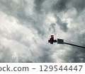 Red traffic light and pedestrian crossing sign against a gloomy cloudy sky. 129544447