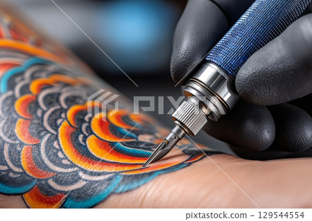 Tattoo artist applying ink with tattoo machine on client's arm 129544554