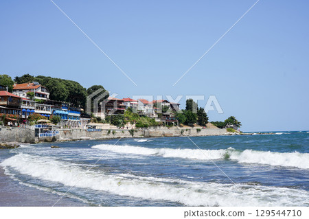 Colorful seaside houses and restaurants line the rocky coast of a picturesque village, with waves Colorful seaside houses and restaurants line the rocky coast of a picturesque village, with waves 129544710