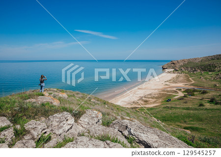 Woman taking photos of seascape and beach from mountain 129545257