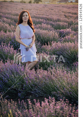 Brunette woman in a white summer dress on a lavender field smiling 129545426