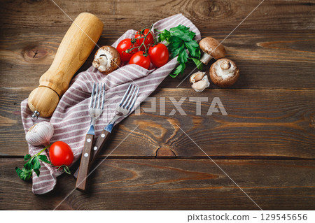 Tomatoes, garlic, champignons, parsley, pepper shaker, forks and napkin on wooden background 129545656