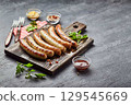 Tasty grilled pork sausages with spice and herbs on wooden cutting board in a close up view on black background. Top view, flat lay. 129545669
