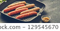 Raw meat sausages on a square grill pan, with herbs and spices. Top view 129545670