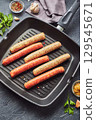Raw meat sausages on a square grill pan, with herbs and spices. Top view 129545671