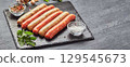 Raw butchers sausages on slate with herbs. Overhead view 129545673