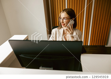 A Professional Woman Engaged in a Productive Phone Call at Her WellOrganized Desk A Professional Woman Engaged in a Productive Phone Call at Her WellOrganized Desk 129545919