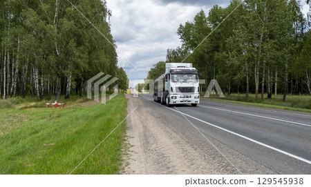 Large White Milk Tanker Drives Along a Highway Through a Forest Landscape Large White Milk Tanker Drives Along a Highway Through a Forest Landscape 129545938