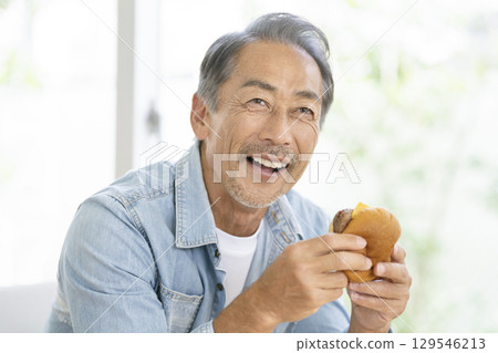 一名 60 多歲的男子正在吃漢堡包 129546213