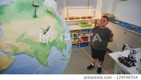 Science Lesson: Primary School Boy Looking at Earth Model with Miniature Wind Turbines and Solar Panels 129546554