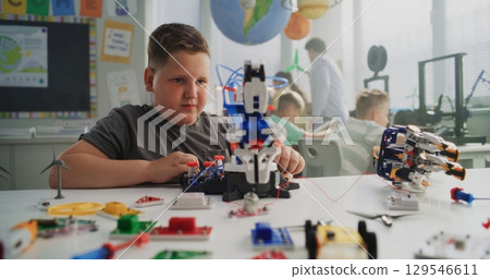 Talented Young Boy Sitting at the Desk, Studying Robotic Arm Model Talented Young Boy Sitting at the Desk, Studying Robotic Arm Model 129546611