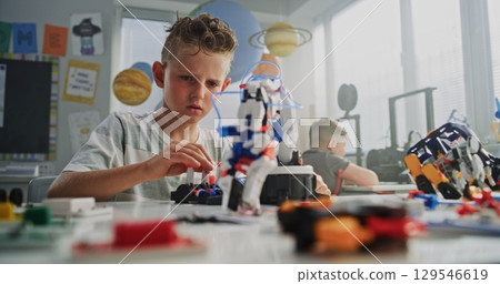 Elementary School Boy Sitting at the Desk, Examining Model of Innovative Robotic Arm 129546619