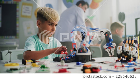 Talented Young Boy Sitting at the Desk, Studying Robotic Arm Model with Male Teacher Talented Young Boy Sitting at the Desk, Studying Robotic Arm Model with Male Teacher 129546625