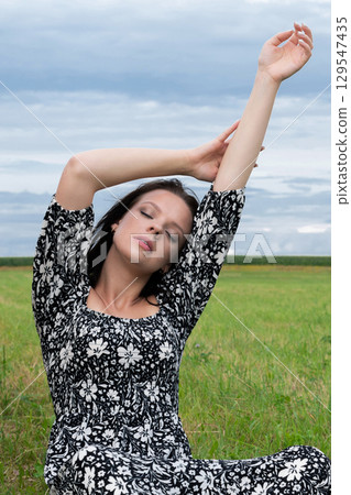 Tranquil Woman in a Floral Dress Meditating in a Field 129547435