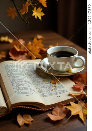 Open book, cup of coffee and autumn leaves resting on wooden table 129547870