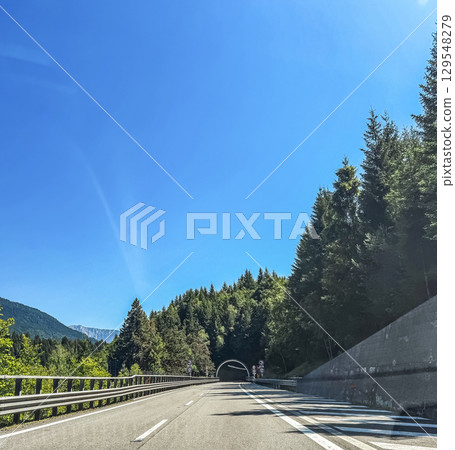 Scenic highway view with a tunnel entrance surrounded by pine forests and mountains under a bright blue sky. High quality photo Scenic highway view with a tunnel entrance surrounded by pine forests and mountains under a bright blue sky. High quality photo 129548279