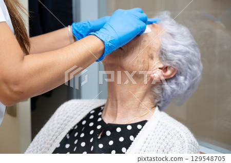 Nurse applying a Medical eye patch to an unrecognizable senior woman 129548705