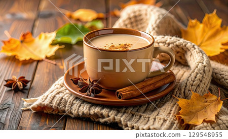 A cup of coffee with cinnamon and a leaf on a table. Scene is cozy and warm 129548955