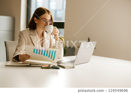 A focused businesswoman is thoroughly analyzing data within a modern office environment A focused businesswoman is thoroughly analyzing data within a modern office environment 129549696