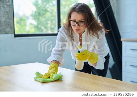 Woman in gloves with a rag and cleaning spray wiped the table Woman in gloves with a rag and cleaning spray wiped the table 129550299