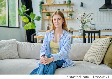 Portrait beautiful smiling young woman at home looking at camera sitting on sofa Portrait beautiful smiling young woman at home looking at camera sitting on sofa 129550371
