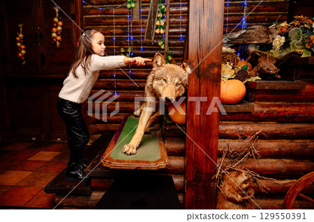 Little girl pointing at stuffed wolf in rustic log cabin Little girl pointing at stuffed wolf in rustic log cabin 129550391
