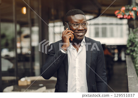 African man. Guy in a black suit. Male with a mobile phone. Businessman at the office. 129551037