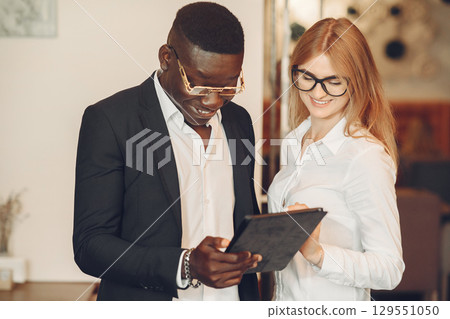 African man. Guy in a black suit. Students with a talet. Girl in white blouse. International people in a cafe. 129551050