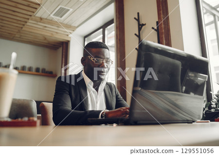 African man. Guy in a black suit. Male with a laptop. Businessman at the office. African man. Guy in a black suit. Male with a laptop. Businessman at the office. 129551056