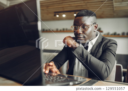 African man. Guy in a black suit. Male with a laptop. Businessman at the office. African man. Guy in a black suit. Male with a laptop. Businessman at the office. 129551057