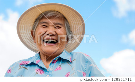 Elderly Woman Smiles Brightly Under a Clear Blue Sky in a Vibrant Floral Shirt 129551711