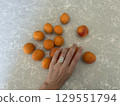 Hand with oval diamond ring arranging apricots on gray stone. 129551794