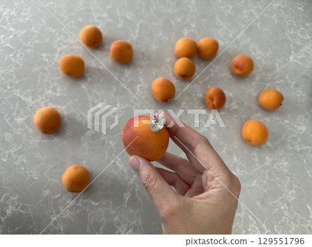 Hand holding apricot with oval diamond engagement ring Hand holding apricot with oval diamond engagement ring 129551796
