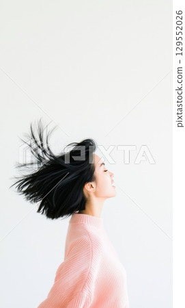 Woman in pink sweater enjoying carefree moment, windswept hair against white backdrop, expressing pure joy and liberation 129552026