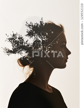 Silhouetted female figure blending with tree branches, creating dreamlike double exposure portrait highlighting human nature interconnectedness and environmental harmony 129552110