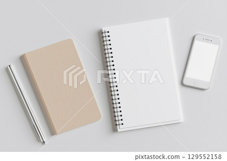 Minimalist white workspace featuring blank spiral notepad, smartphone, writing pen positioned on clean surface, overhead perspective 129552158