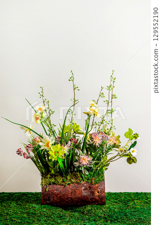 Colorful arrangement of artificial flowers displayed in a rustic wooden planter on a grassy surface 129552190