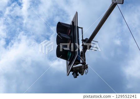 Modern traffic light showing a bright green signal illuminated against a dynamic cloudy blue sky, symbolizing regulation, safe urban flow, and permission to proceed 129552241