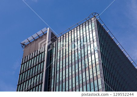 Modern high-rise office building, its reflective glass facade gleaming under a bright blue sky, represents urban business and architectural progress Modern high-rise office building, its reflective glass facade gleaming under a bright blue sky, represents urban business and architectural progress 129552244