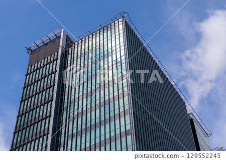 Sleek glass facade of a modern skyscraper stands tall against a vibrant blue sky, symbolizing corporate success, urban development, and contemporary architectural design Sleek glass facade of a modern skyscraper stands tall against a vibrant blue sky, symbolizing corporate success, urban development, and contemporary architectural design 129552245