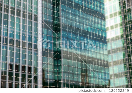 Protective mesh net forms a clean geometric grid pattern against a blurred modern glass building, conveying urban safety and contemporary architecture Protective mesh net forms a clean geometric grid pattern against a blurred modern glass building, conveying urban safety and contemporary architecture 129552249